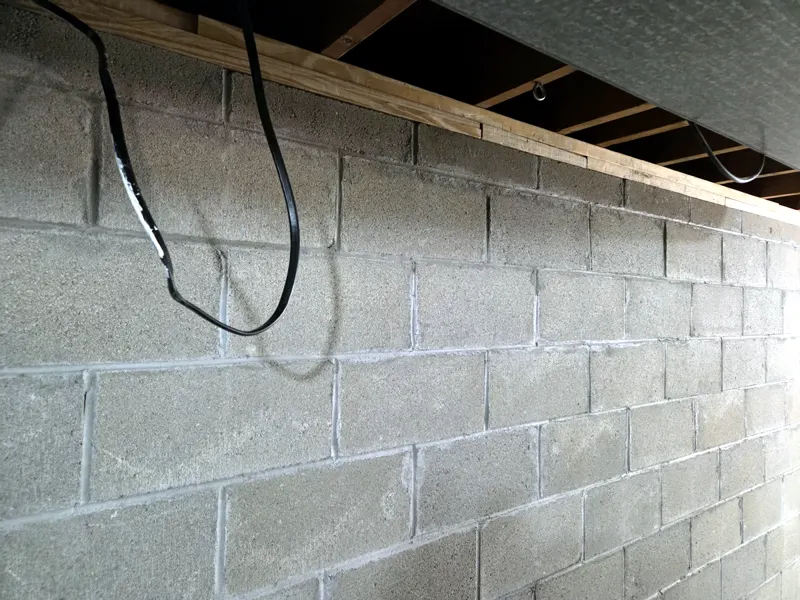 Bare concrete block basement wall below the wood sill plate and floor framing