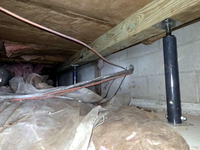 Adjustable steel support jack installed under a crawl space beam beside a block wall
