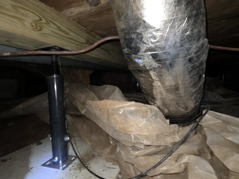 Steel support jack set on a base plate under a beam next to crawl space ductwork
