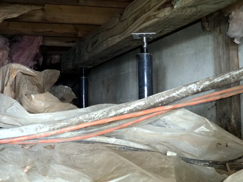 Row of adjustable steel support jacks under a crawl space beam along a block wall