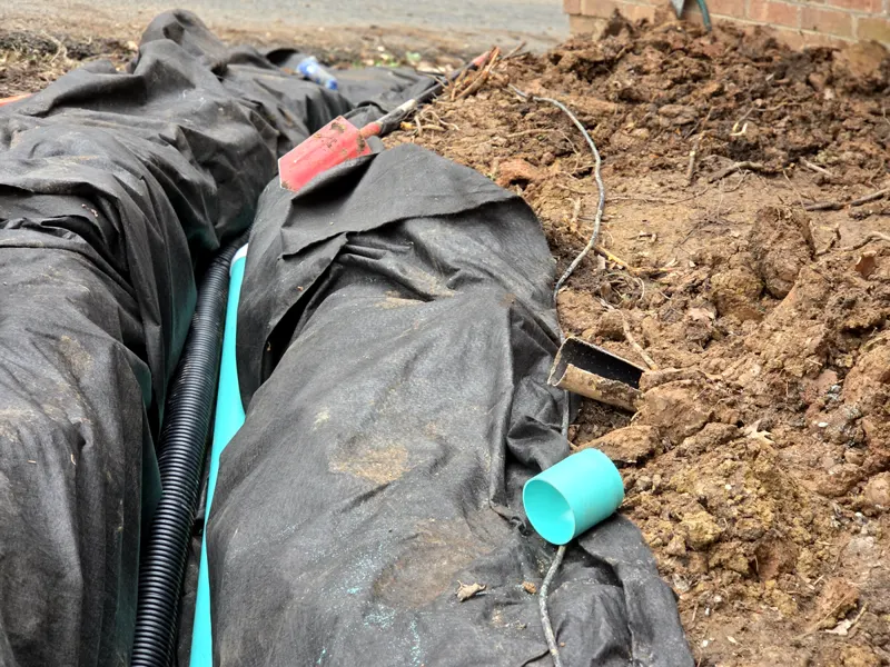 French drain trench lined with filter fabric, with black perforated drain pipe and a green pipe fitting