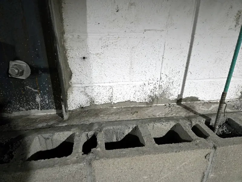 Steel base plate bolted at the top of a concrete block wall, with open block cores exposed during a wall repair